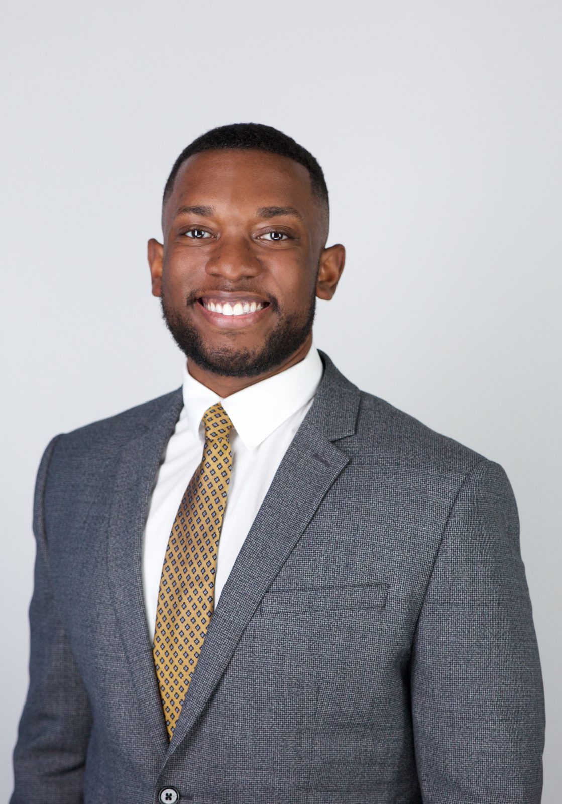ERAS application photo example — applicant in a gray suit with a small-pattern gold tie, composed expression, New York studio