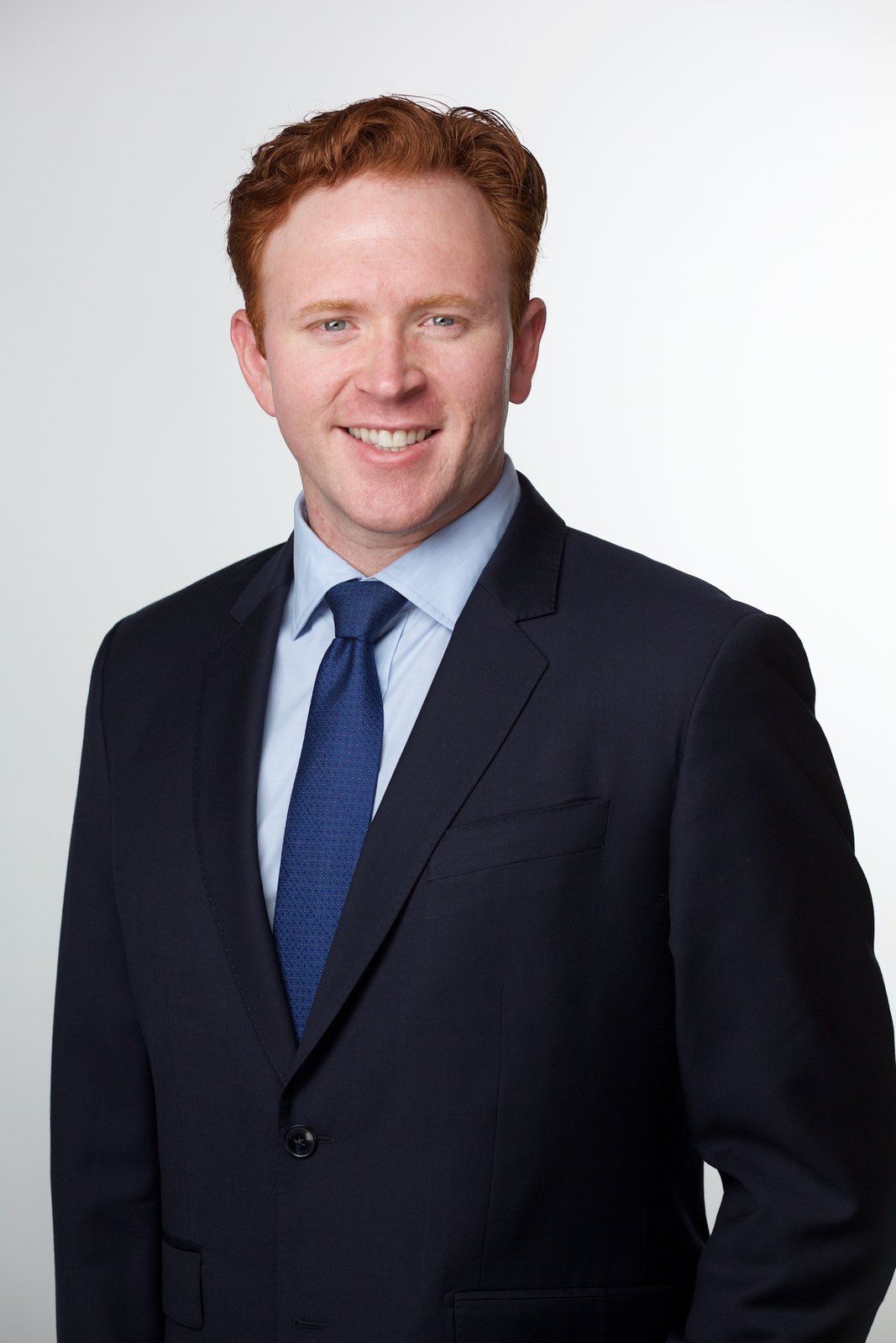 ERAS application photo example — applicant in navy suit and blue tie, direct gaze on a light gray background